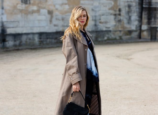 A woman wears a trench coat and black handbag at Paris Fashion Week