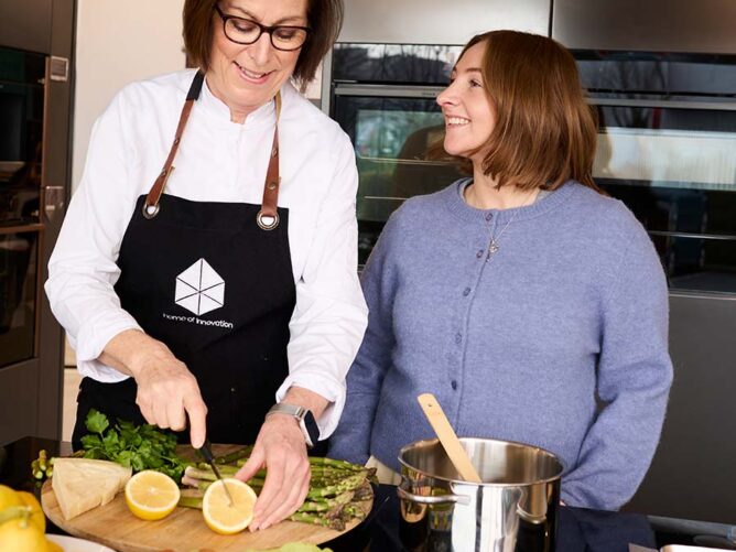 two women in a kitchen smiling and cutting fruit