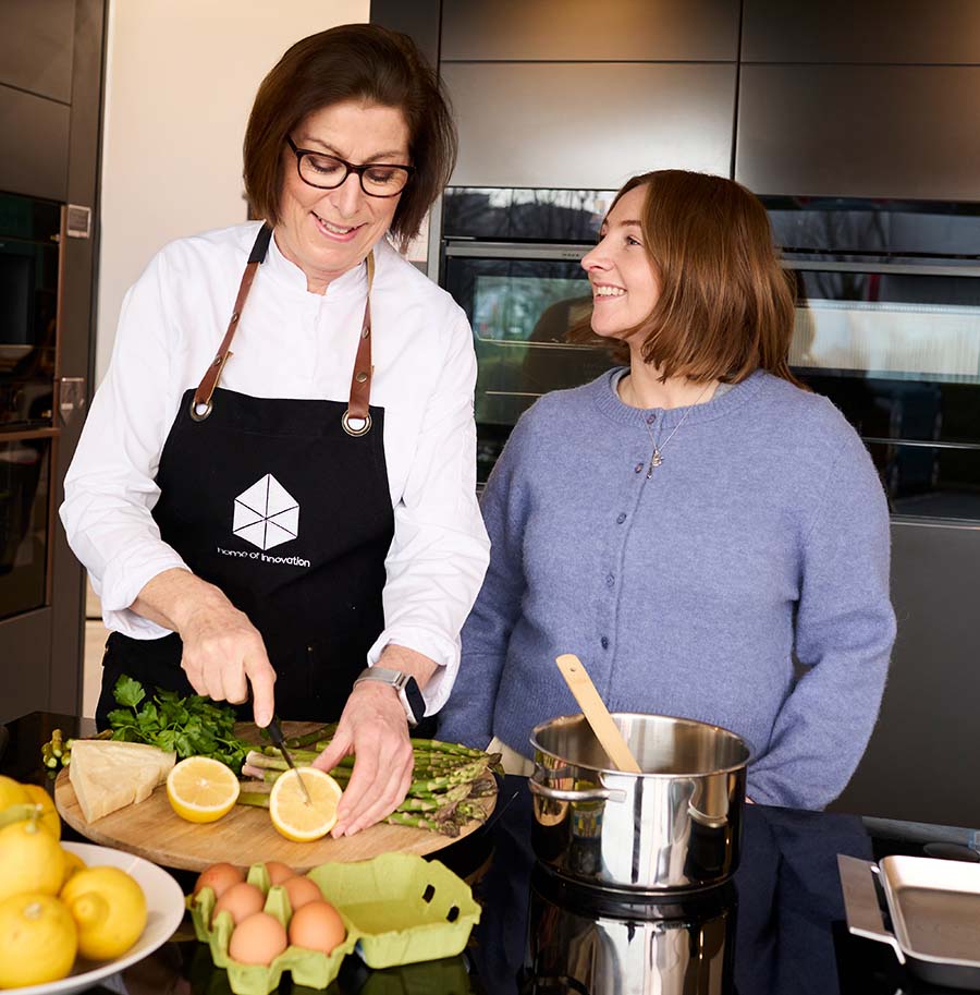 two women in a kitchen smiling and cutting fruit